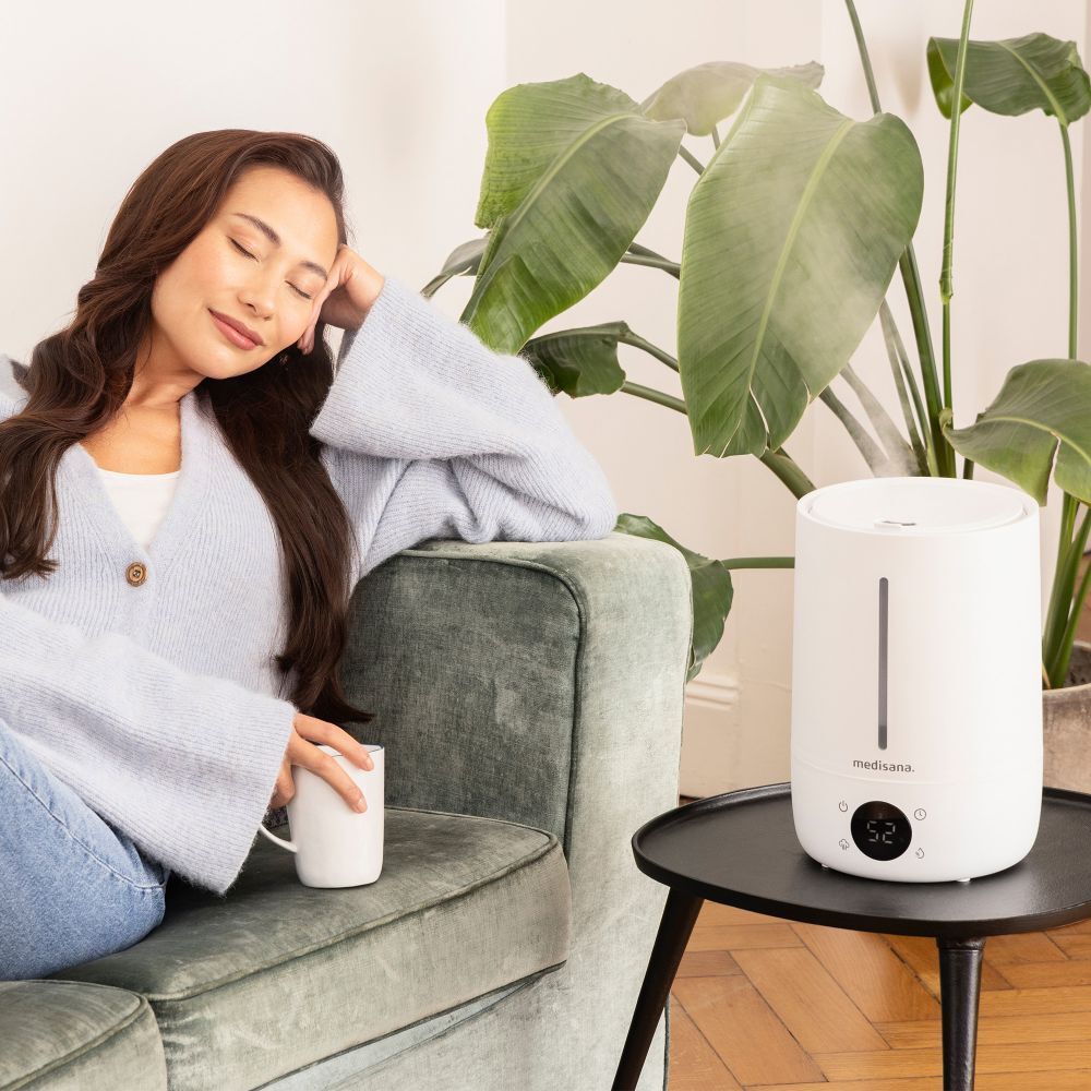 Humidificateur blanc sur une table. Femme assise sur un canapé. Marque : medisana.