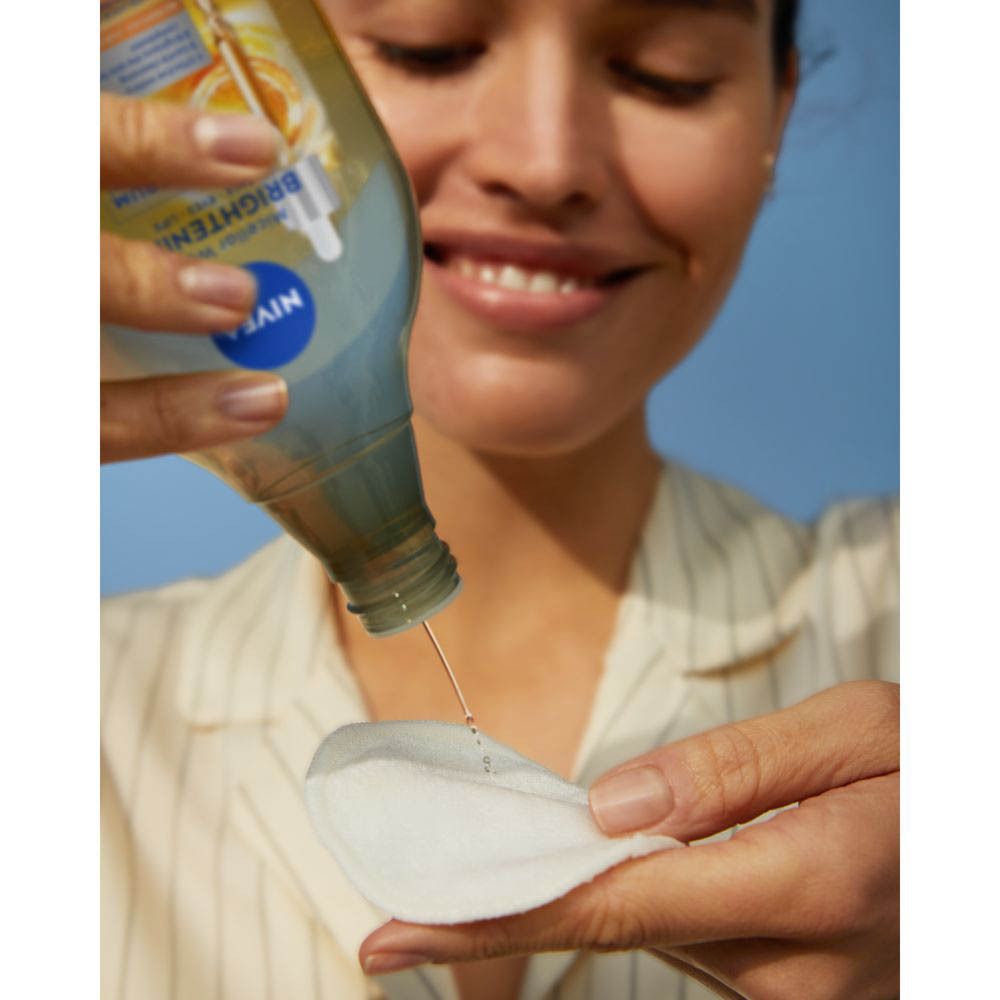 Femme versant Nivea Skin Glow Eau Micellaire sur un coton démaquillant. Sourire.