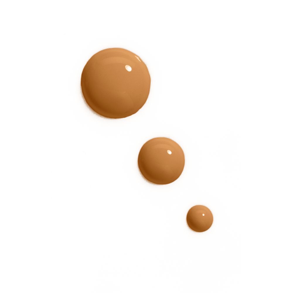 Trois gouttes de fond de teint de différentes teintes marron sur fond blanc.