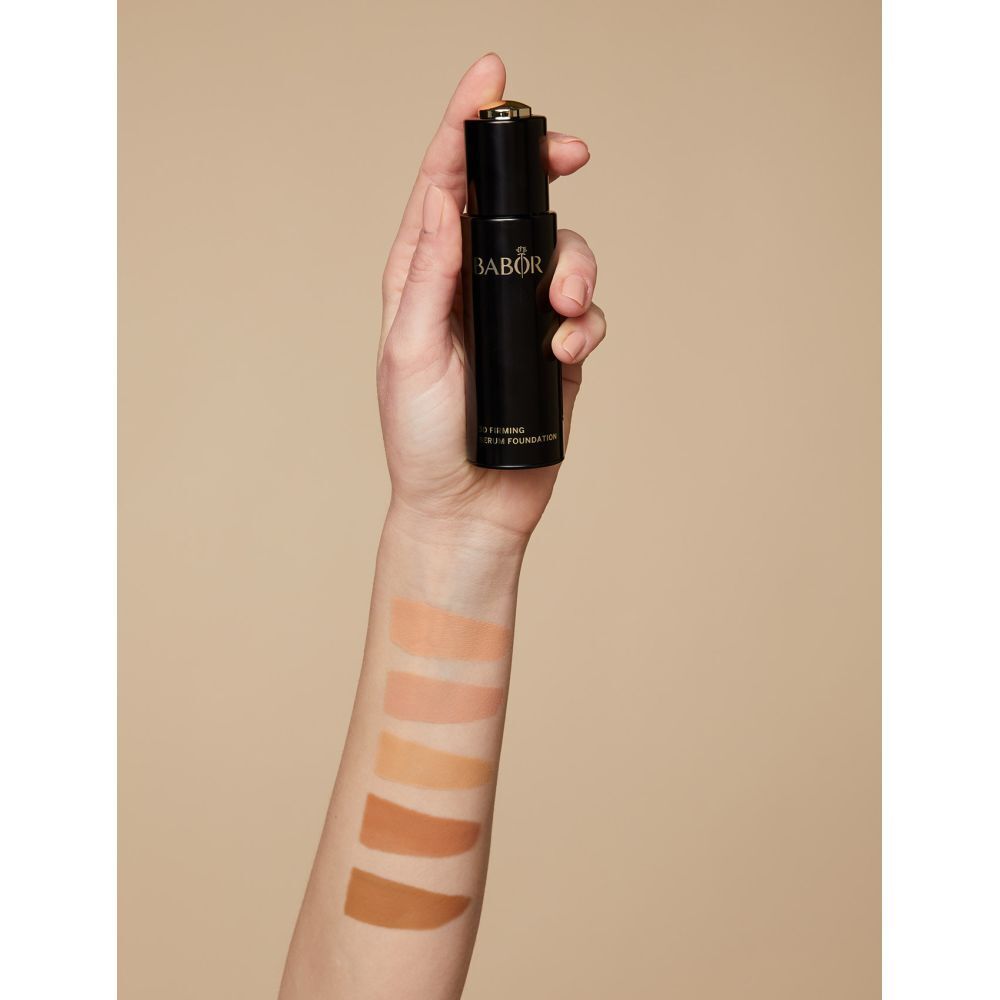 Main tenant un flacon. Échantillons de couleurs appliqués sur le bras. Inscription: BABOR, 3D Firming Serum Foundation.