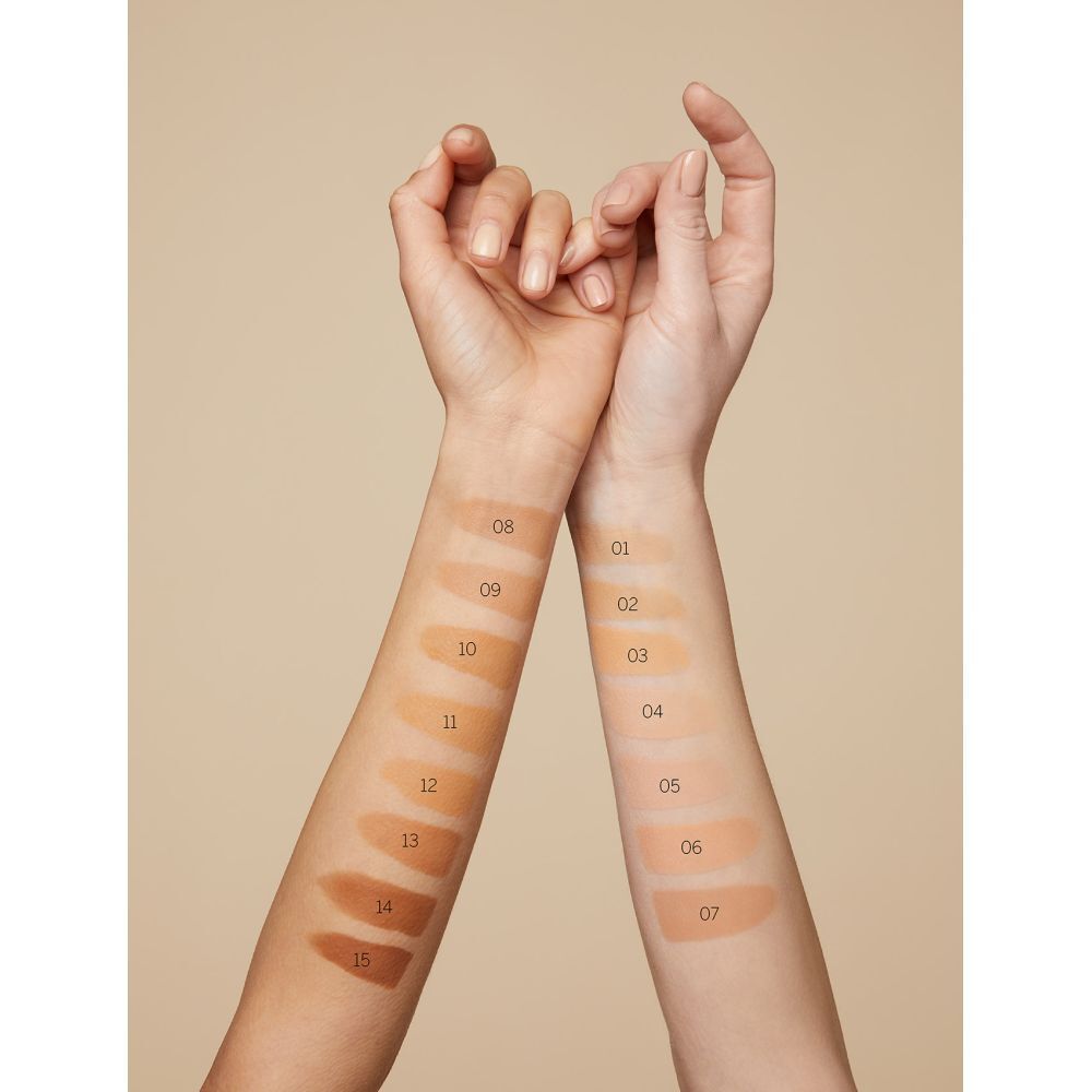 Bras avec échantillons de fond de teint. Numéros de teinte 08-15 sur une main, 01-07 sur l'autre. Fond beige.