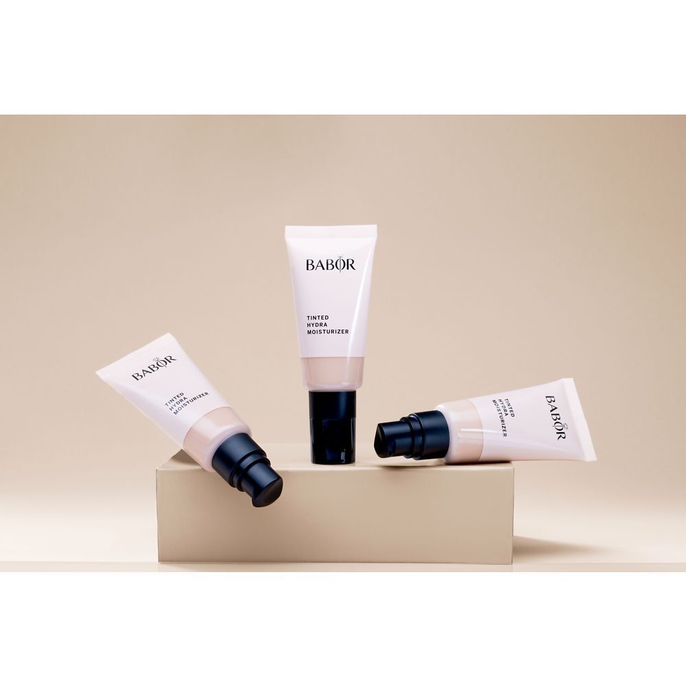 Trois tubes BABOR® Tinted Hydra Moisturizer. Un debout, deux couchés. Inscription: BABOR, TINTED HYDRA MOISTURIZER.