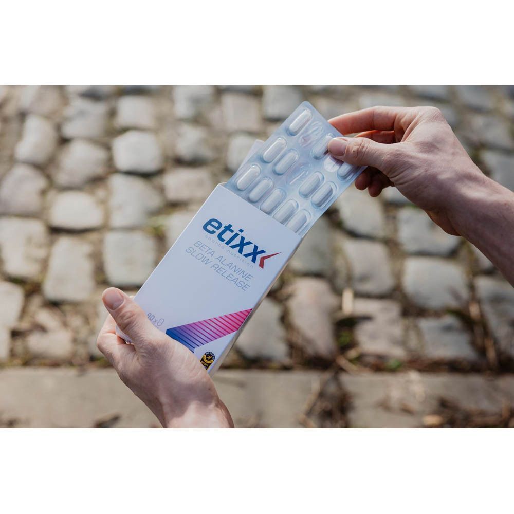 Mains ouvrant une boîte d'Etixx Beta Alanine Slow Release, révélant des plaquettes de comprimés.