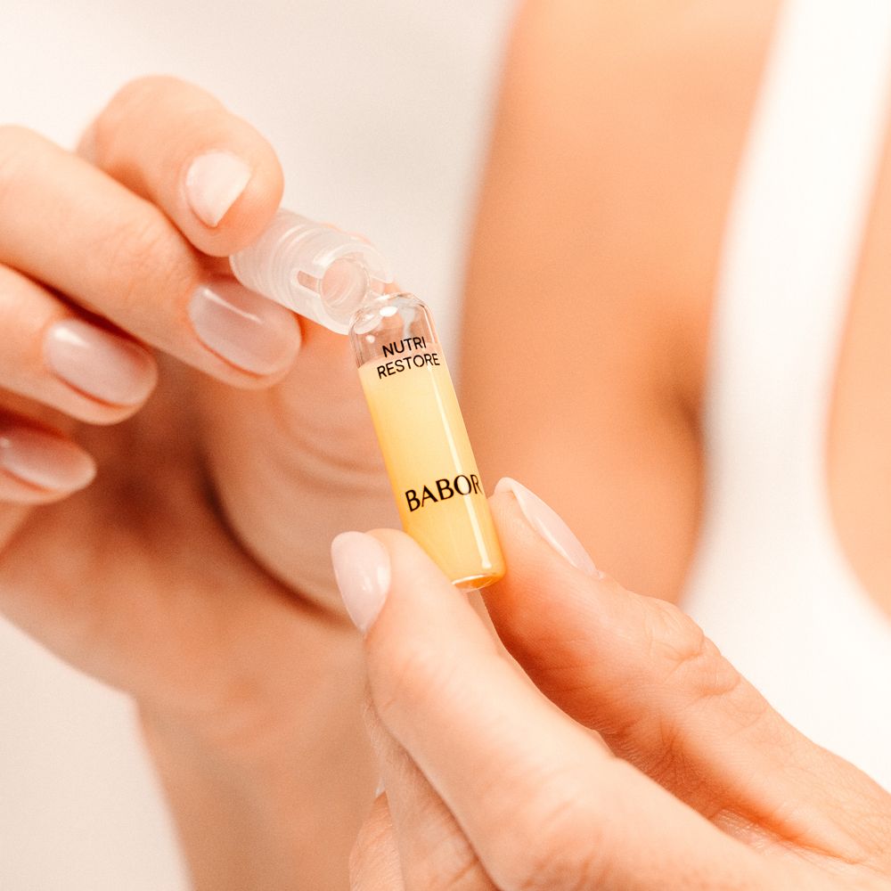Mains tenant une ampoule. Texte : Nutri Restore, Babor.