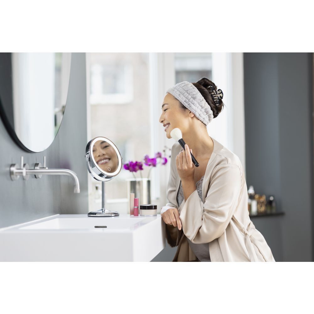 Femme utilisant un miroir cosmétique. La femme se maquille. Miroir, lavabo, salle de bain.