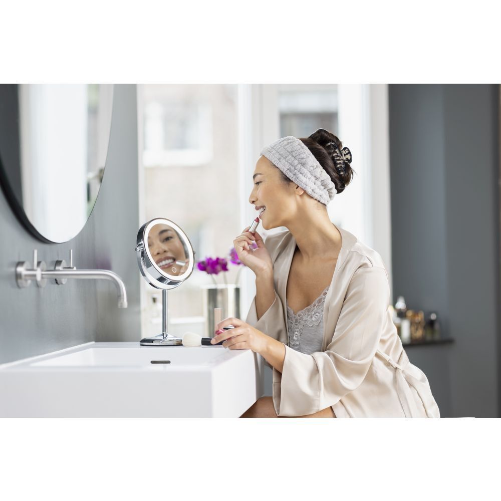 Femme utilisant un miroir cosmétique. La femme se maquille. Miroir, lavabo, salle de bain.