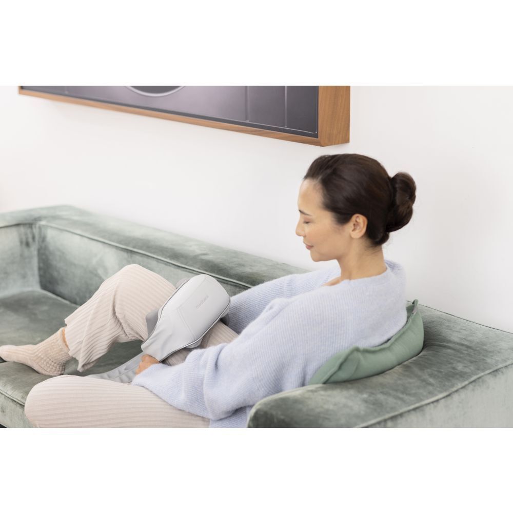 Femme assise sur un canapé, masseur de cou sur la jambe. Masseur gris.