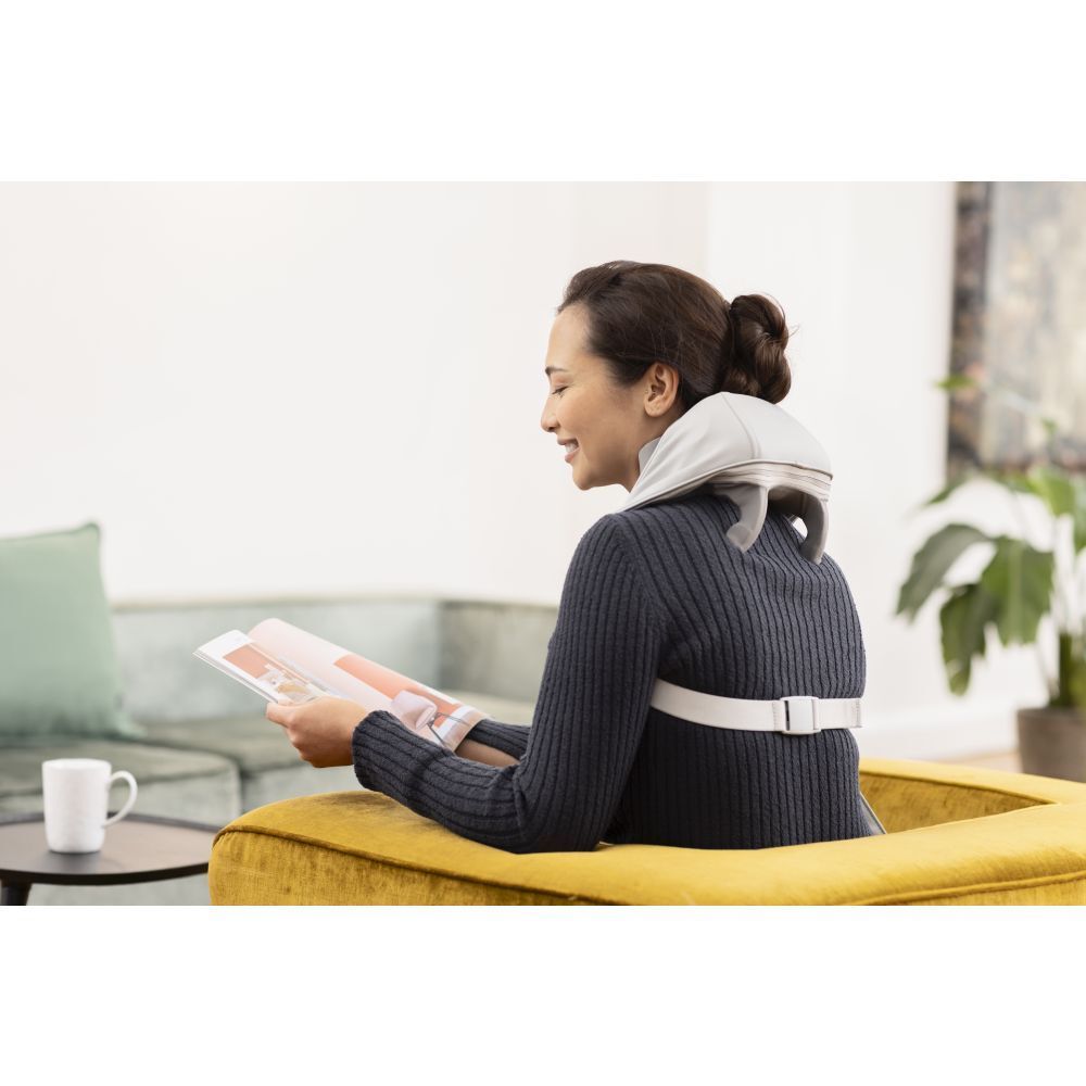 Femme assise sur un canapé, masseur de cou. Masseur gris. Lit un livre.