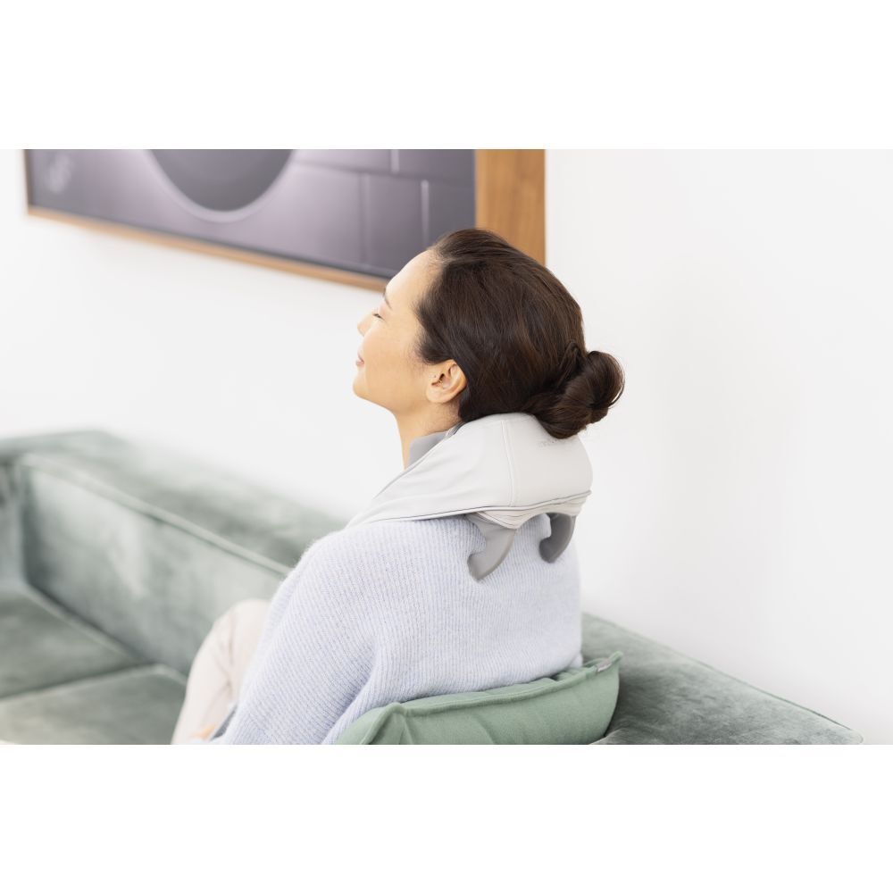 Femme assise sur un canapé, masseur de cou. Masseur gris. Détendue.