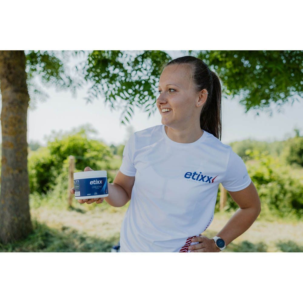 Une femme tient une boîte à étiquette bleue. Inscription : Etixx. Elle porte un t-shirt blanc avec le logo Etixx.