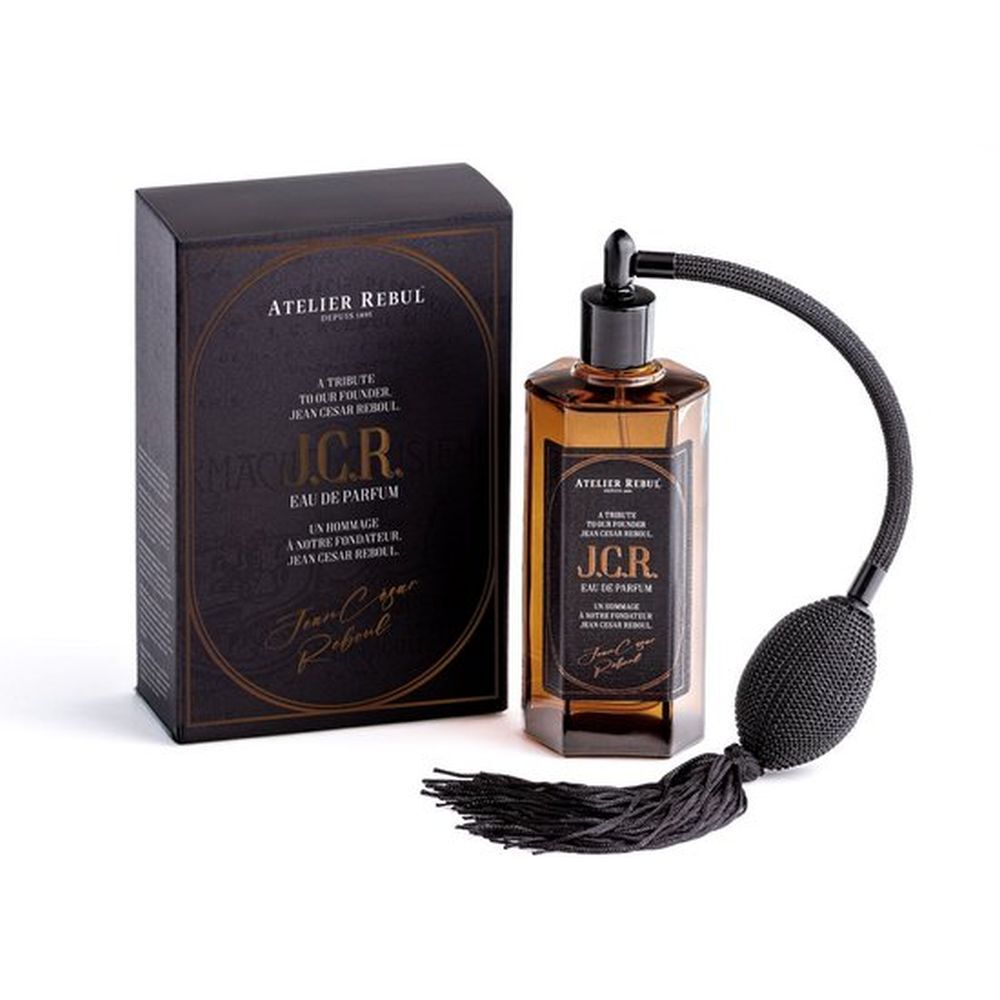 Flacon de parfum et boîte. Flacon avec vaporisateur. Boîte noire avec cadre doré. Texte: Atelier Rebul, J.C.R. Eau de Parfum.