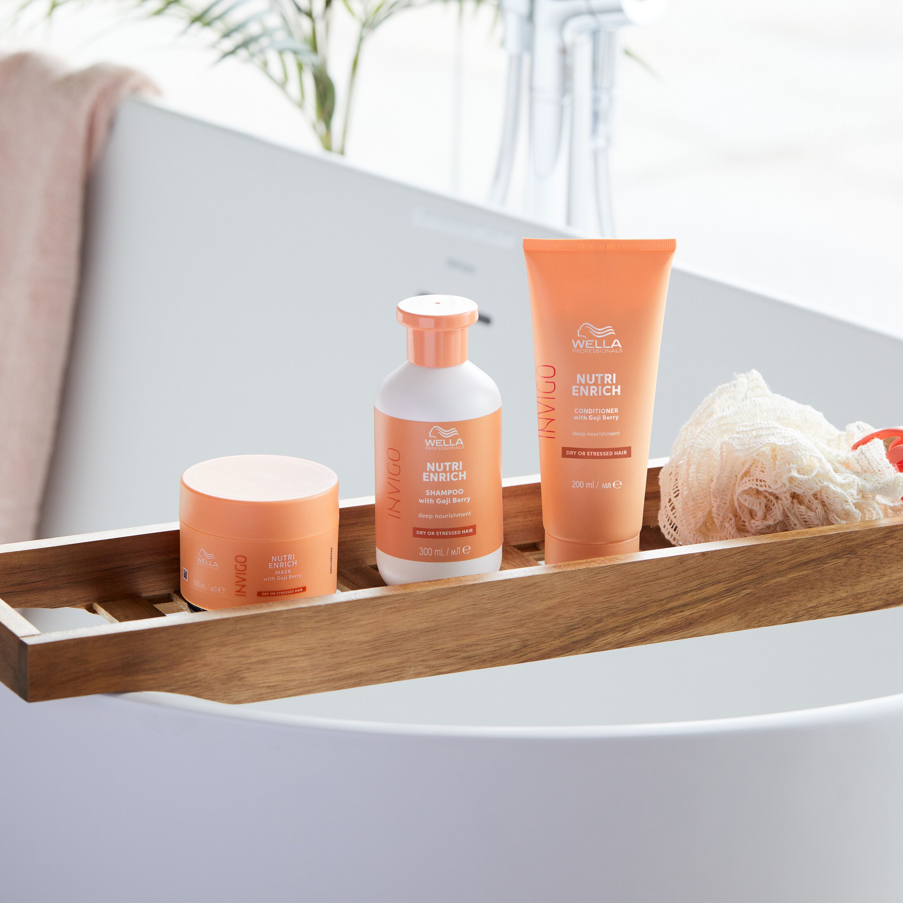 Trois produits sur un plateau en bois dans une baignoire. Un pot, une bouteille et un tube.
