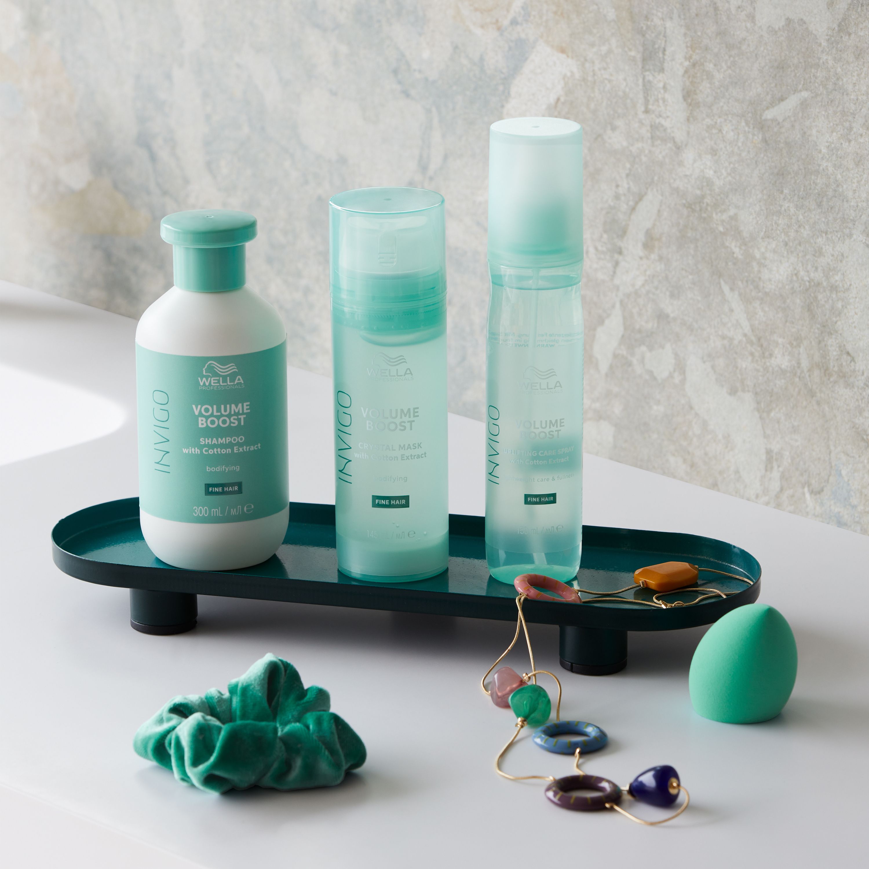 Arrangement de produits avec trois produits Wella Invigo, bijoux et accessoires sur un plateau.