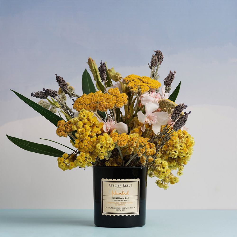 Bougie parfumée noire dans un verre, décorée d'un bouquet de fleurs séchées.