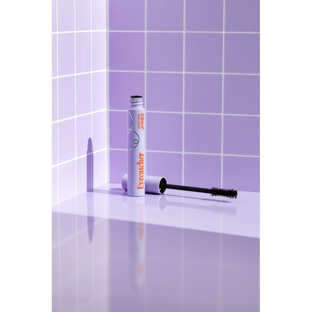 Tube et brosse de mascara dans un environnement lilas. Tube lilas avec lettrage orange 'Eyecatcher'.
