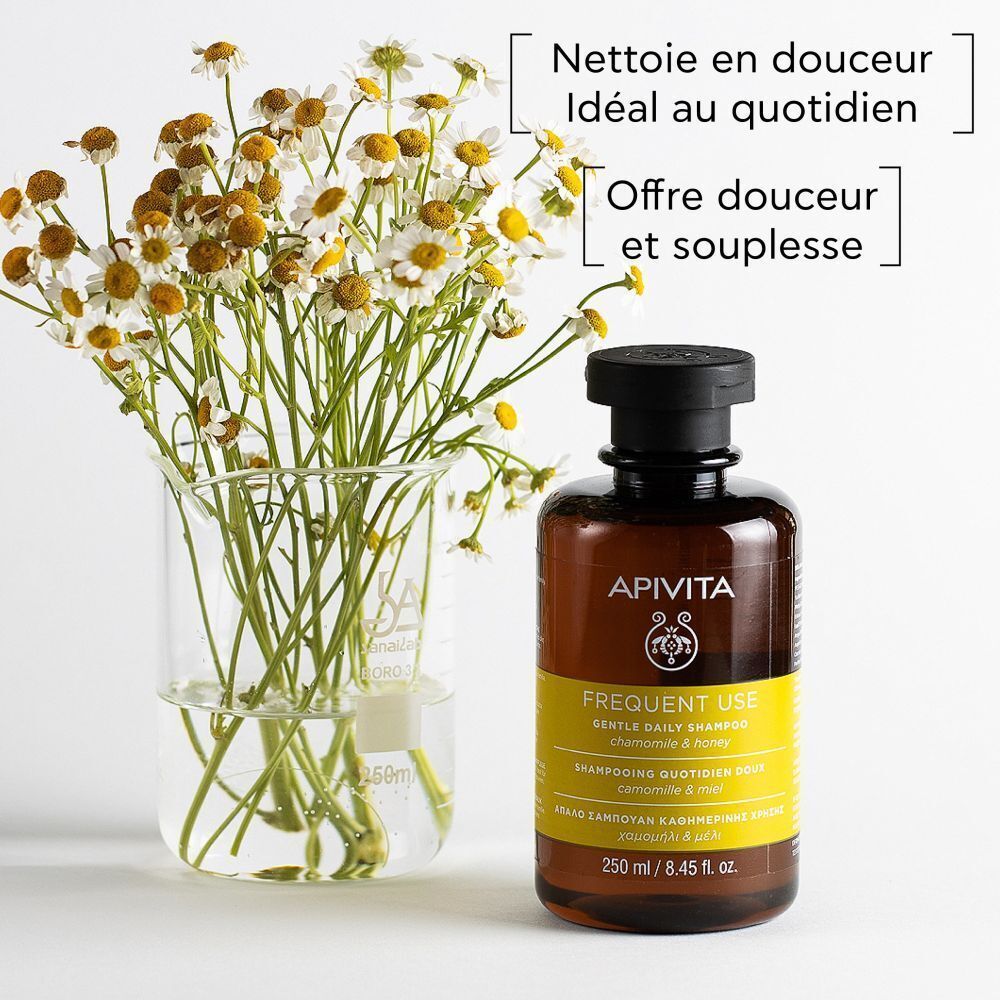 Flacon de shampooing à côté de fleurs de camomille dans un bécher. Texte : Nettoie en douceur, Idéal au quotidien, Offre douceur et souplesse.