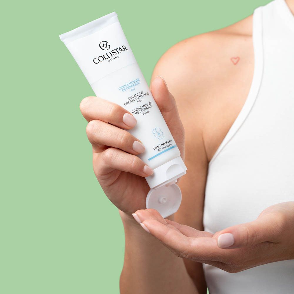 Personne tenant un tube blanc. Le produit est pressé dans la main. Texte : Cleansing Cream To Mousse.