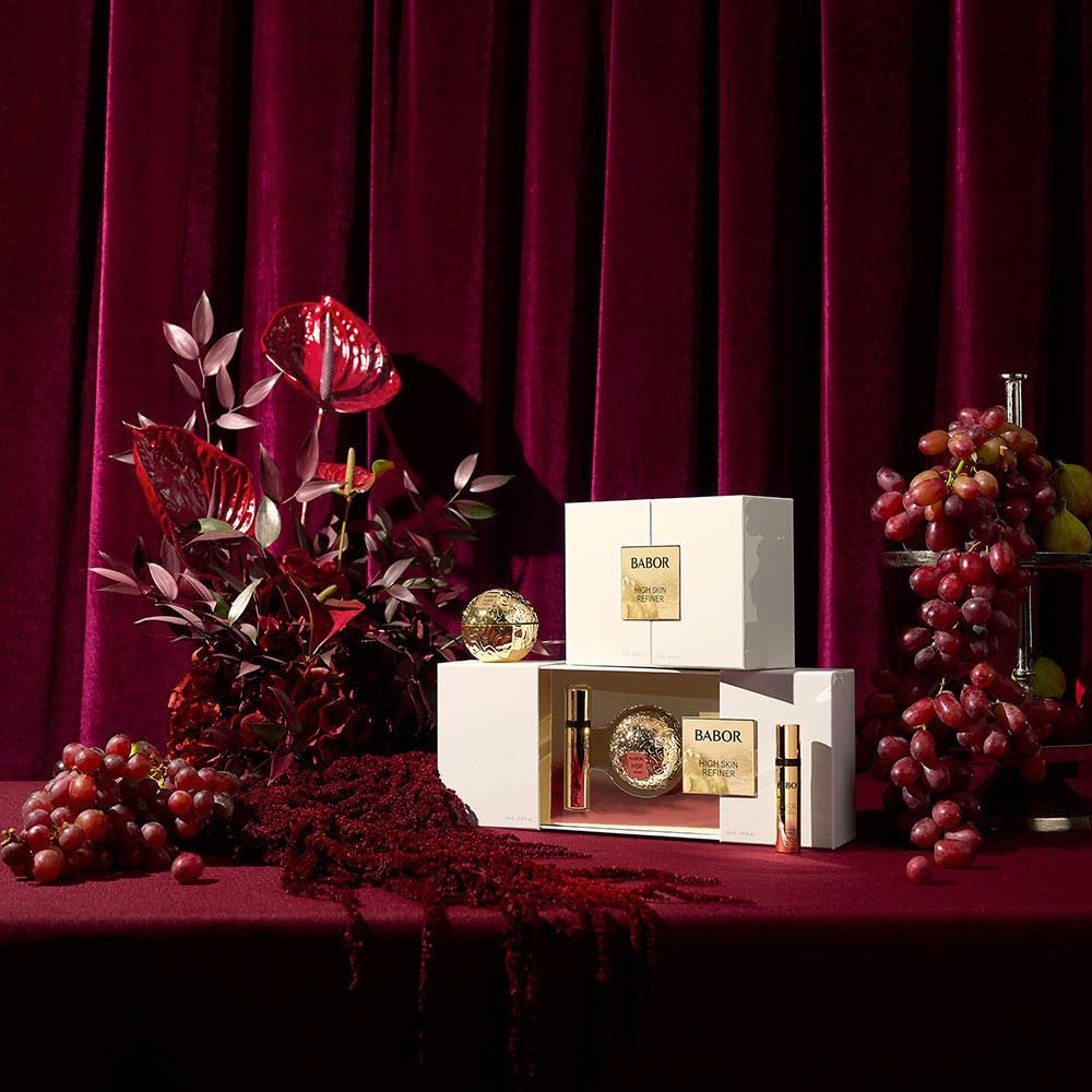 Présentation du produit avec coffrets cadeaux et décoration. Inscription: BABOR HIGH SKIN REFINER. Produits sur table rouge.