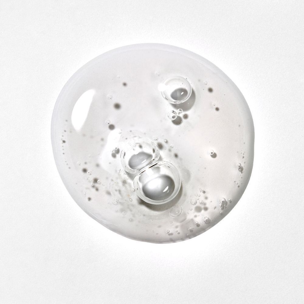 Gros plan d'un liquide clair avec des bulles. Le liquide est étalé sur une surface blanche.