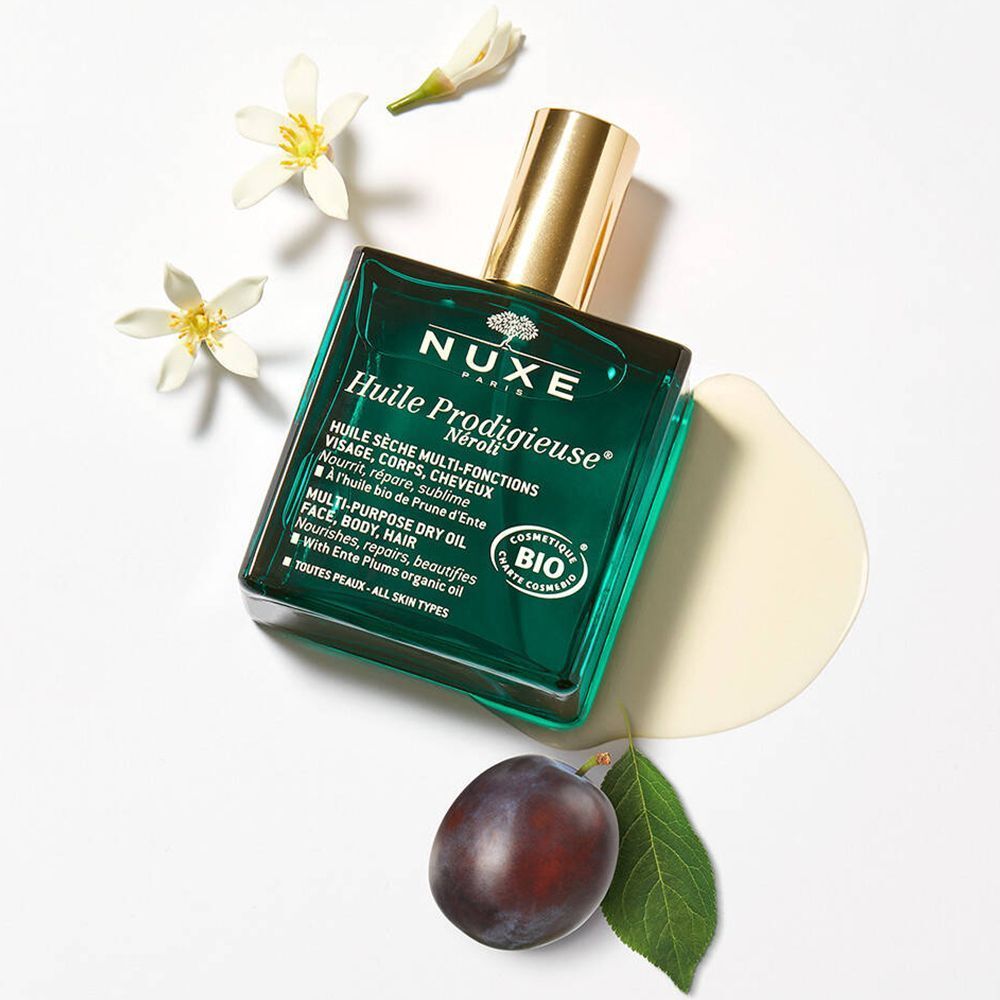 Flacon vert avec bouchon doré, prune et fleurs. Inscription : NUXE Huile Prodigieuse® Neroli Bio.
