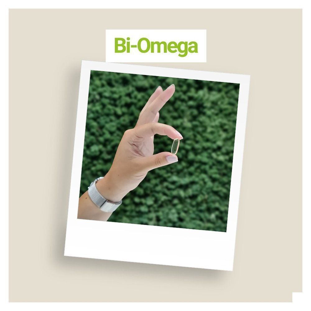 Main tenant une gélule Bi-Omega DHA devant un fond vert.