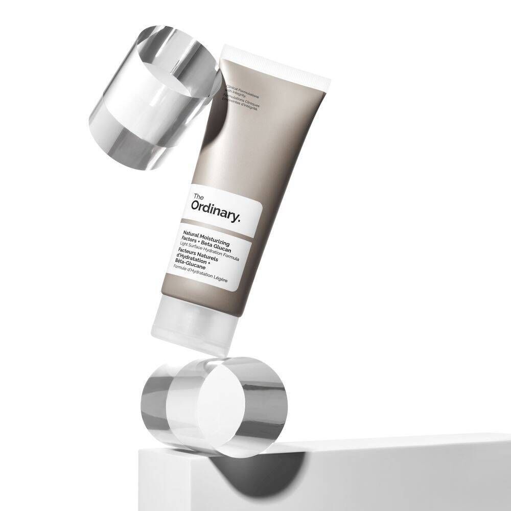 Tube en équilibre avec deux cylindres transparents. Inscription: The Ordinary, Natural Moisturizing Factors + Beta Glucan.