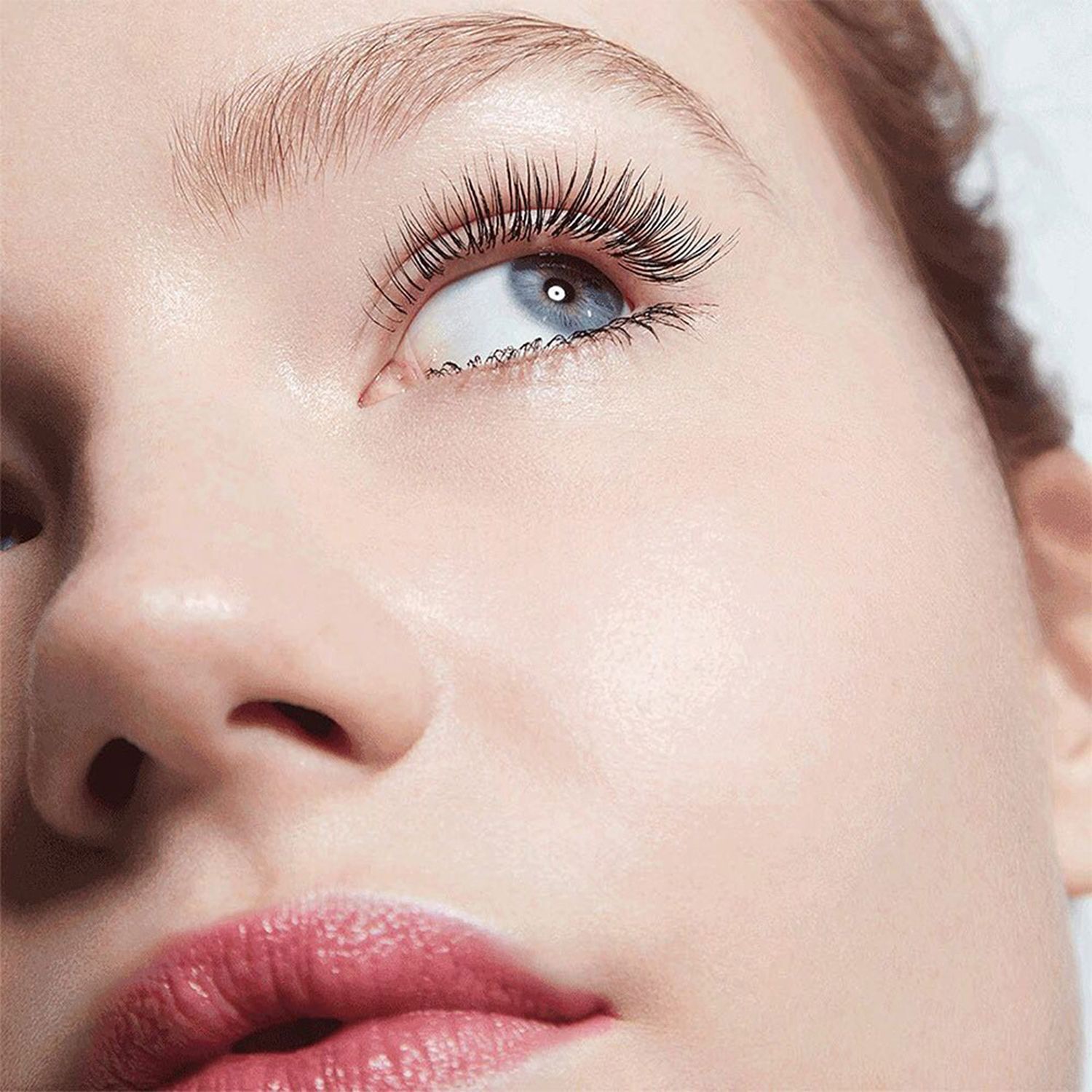 Gros plan d'un visage avec de longs cils maquillés. Rouge à lèvres rouge. Regard vers le haut.