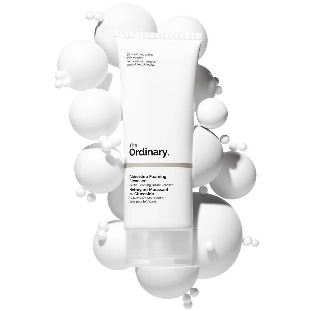 Un tube de The Ordinary Glucoside Foaming Cleanser entouré de sphères blanches.