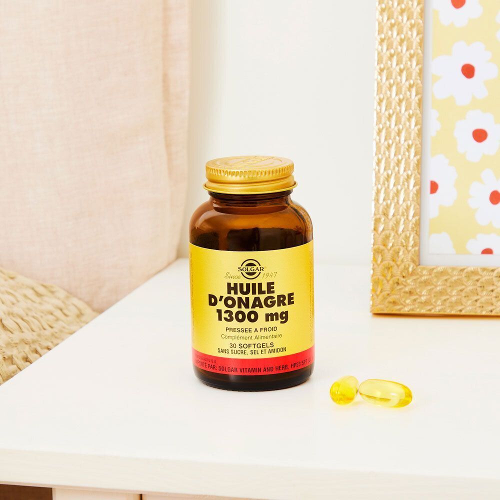 Flacon en verre brun avec bouchon doré et trois gélules sur une surface blanche. Fond : table et image.