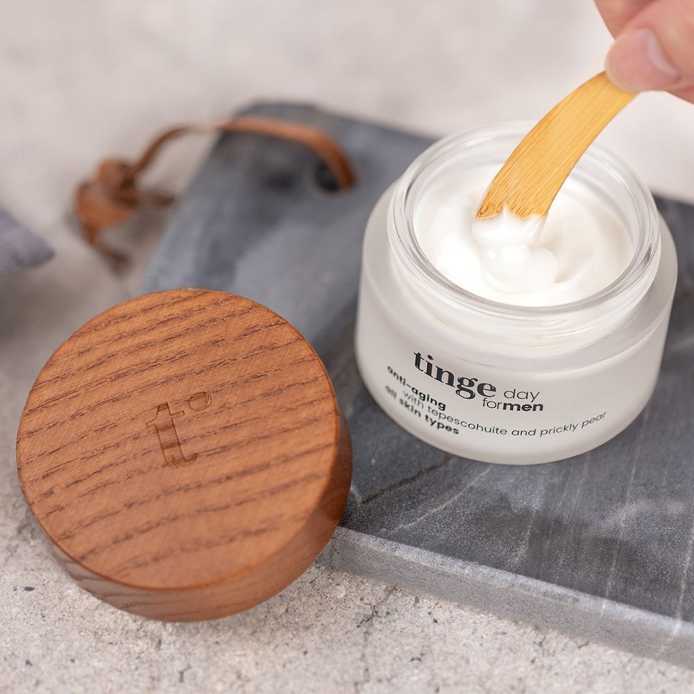 Pot ouvert avec couvercle en bois et cuillère. Inscription: Tinge day for men, anti-âge, avec tepescohuite et figue de barbarie, tous types de peau.