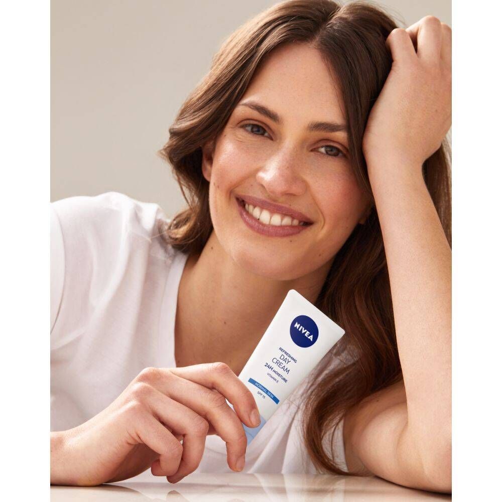 Femme tenant une crème de jour NIVEA. Tube blanc avec logo bleu. Texte: Hydratation 24H. La femme sourit.