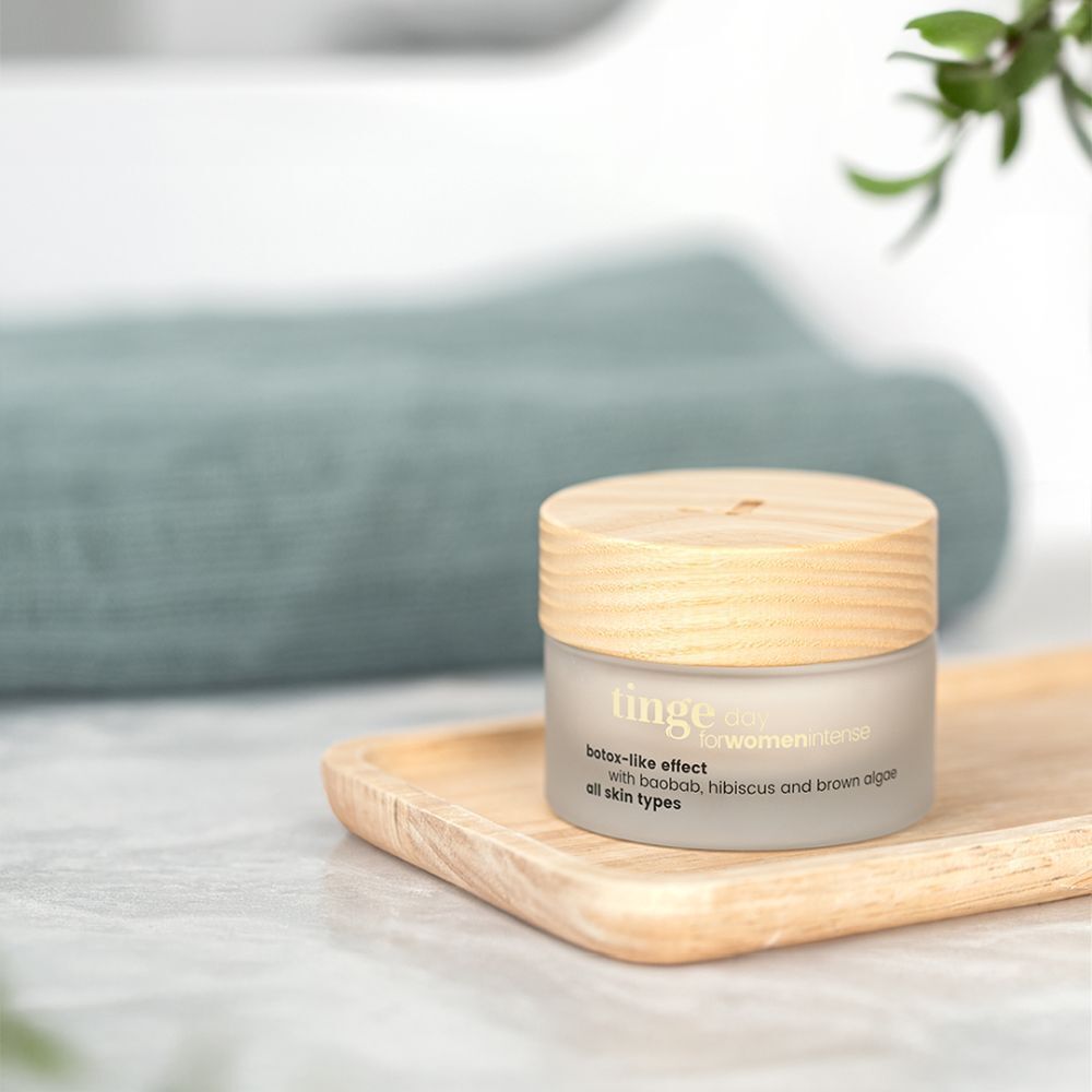 Pot de Crème de Jour Intense sur plateau en bois. Verre blanc, couvercle en bois. Inscription : Tinge, botox-like effect, pour tous types de peau.