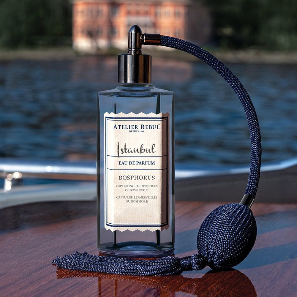 Flacon bleu foncé avec vaporisateur. Inscription: Istanbul Bosphorus Eau De Parfum. Flacon sur bois. Fond: eau.