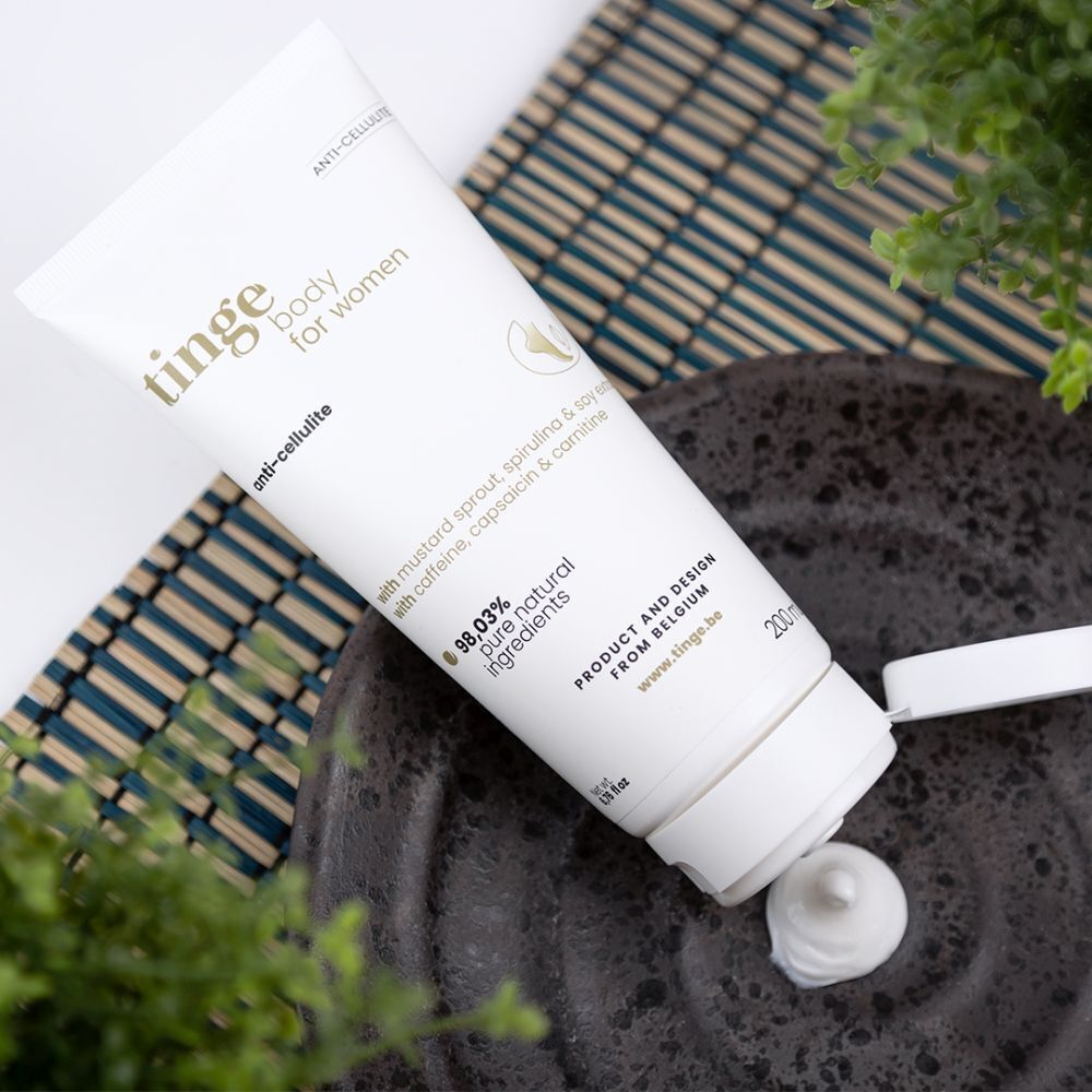 Tube de crème sur fond. Inscription: Tinge body for women, anti-cellulite. Avec ingrédients. 98,03% ingrédients naturels purs. Produit de Belgique.