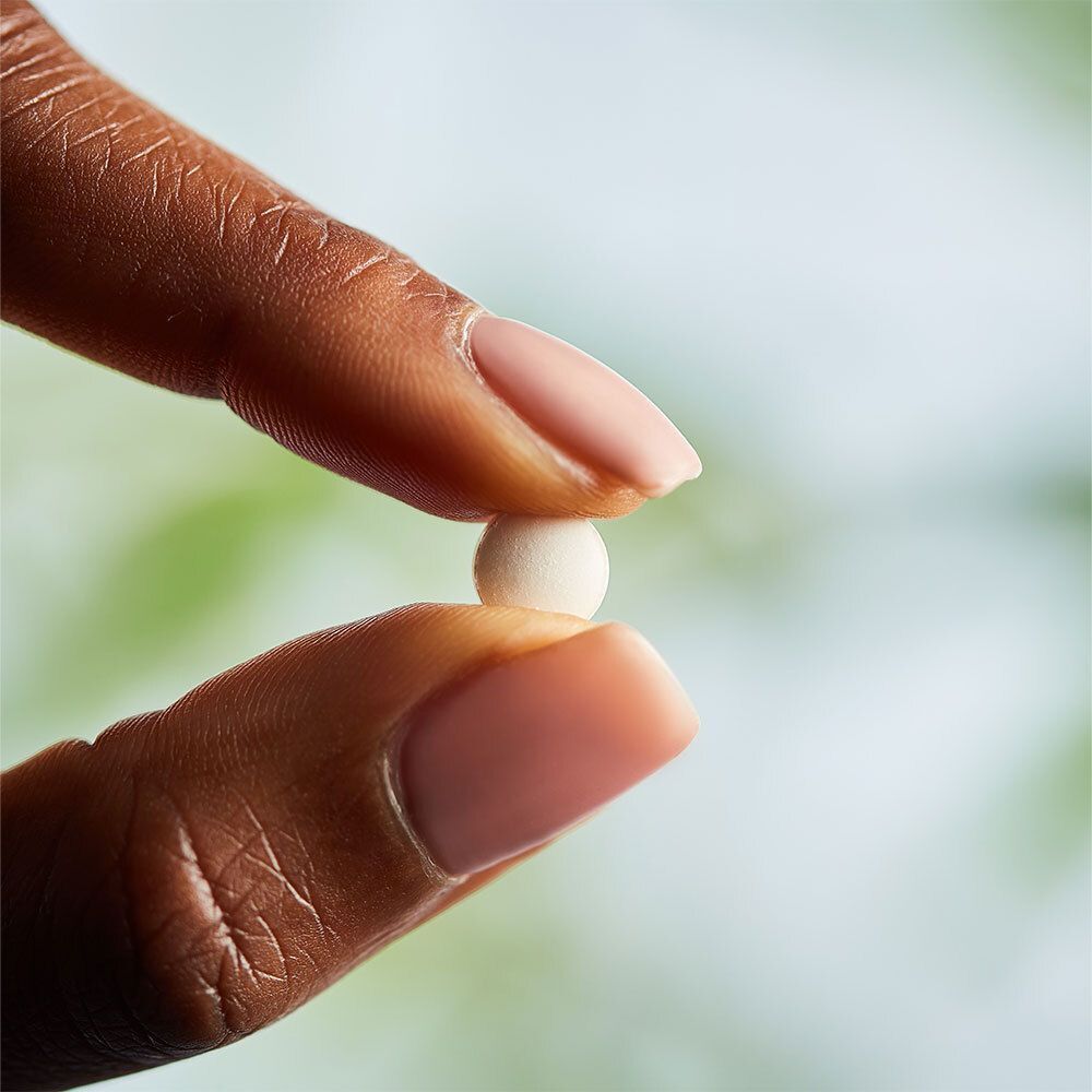 Un comprimé blanc tenu entre deux doigts. Couleur de peau de la personne.
