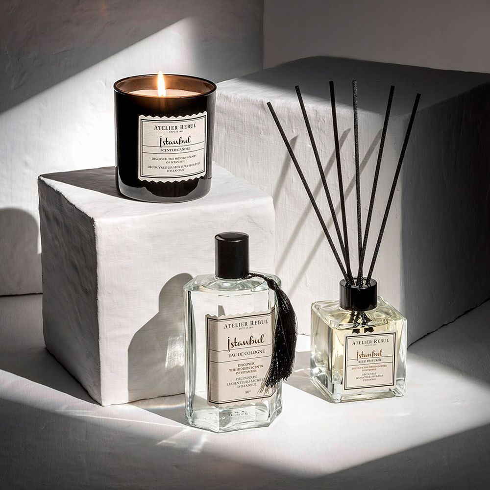 Trois produits ATELIER REBUL : Istanbul Eau de Cologne, bougie parfumée et bâtonnets parfumés. Sur un piédestal blanc.