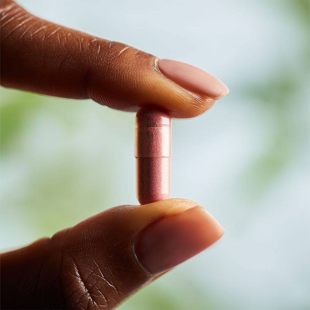 Une gélule rose tenue par une main avec des ongles vernis en rose.