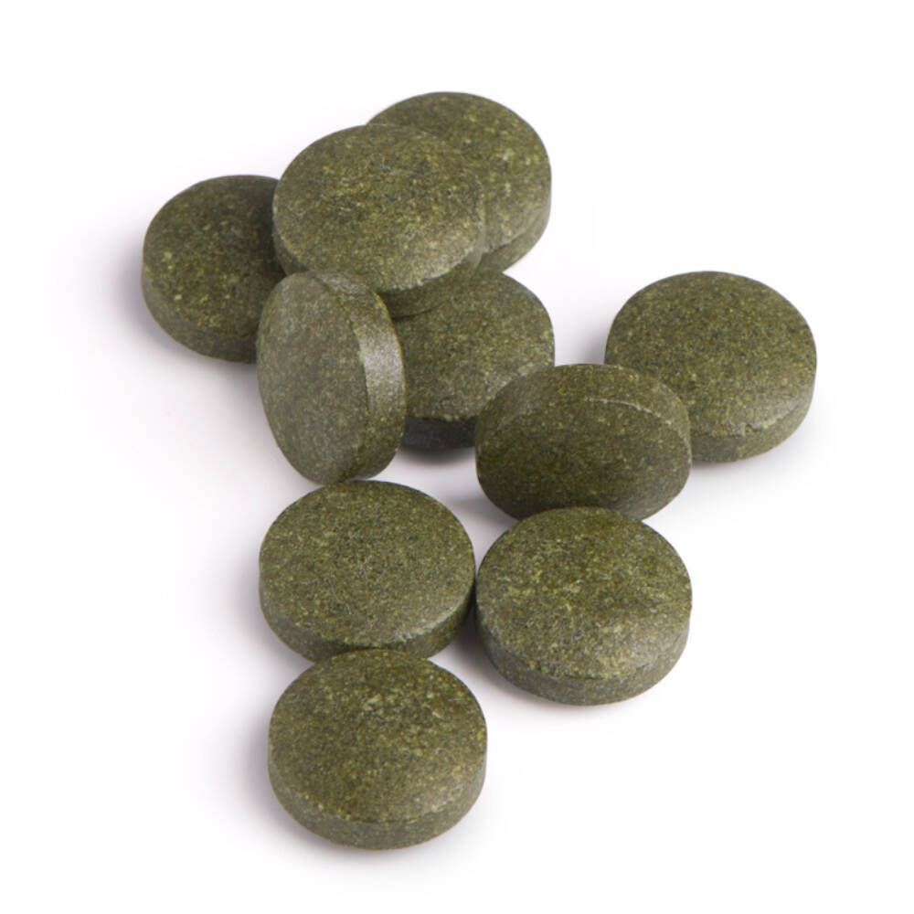 Gros plan sur des comprimés verts et ronds. Certains comprimés sont légèrement ovales. Sur fond blanc.
