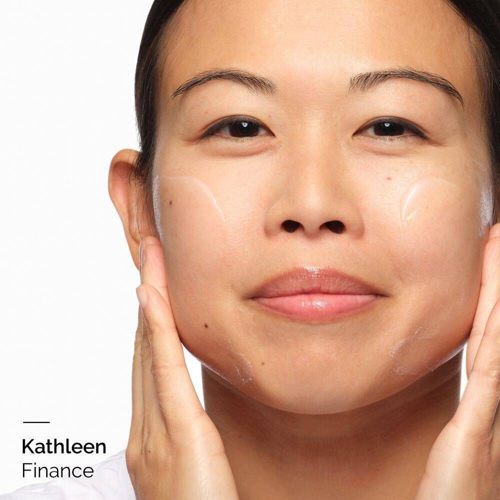 Gros plan d'une personne appliquant de la crème sur son visage. Le nom 'Kathleen Finance' est visible en bas à gauche.
