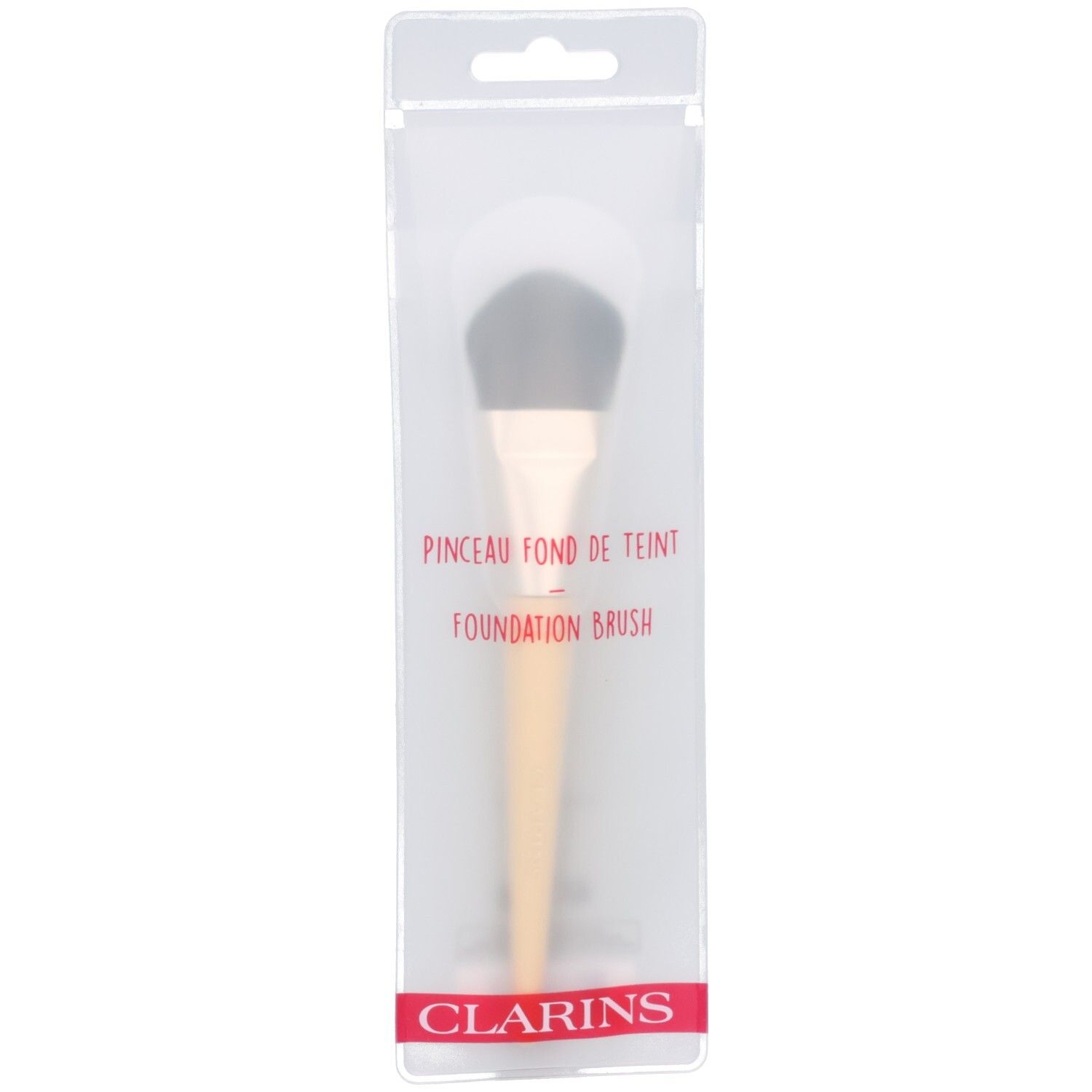Pinceau fond de teint Clarins dans son emballage transparent. Manche clair, poils foncés.