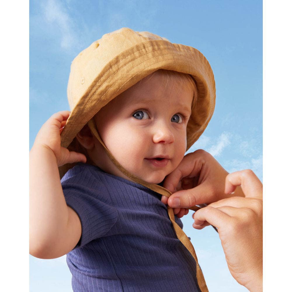 Bébé avec chapeau de soleil, mains attachant le chapeau. Ciel bleu en arrière-plan.