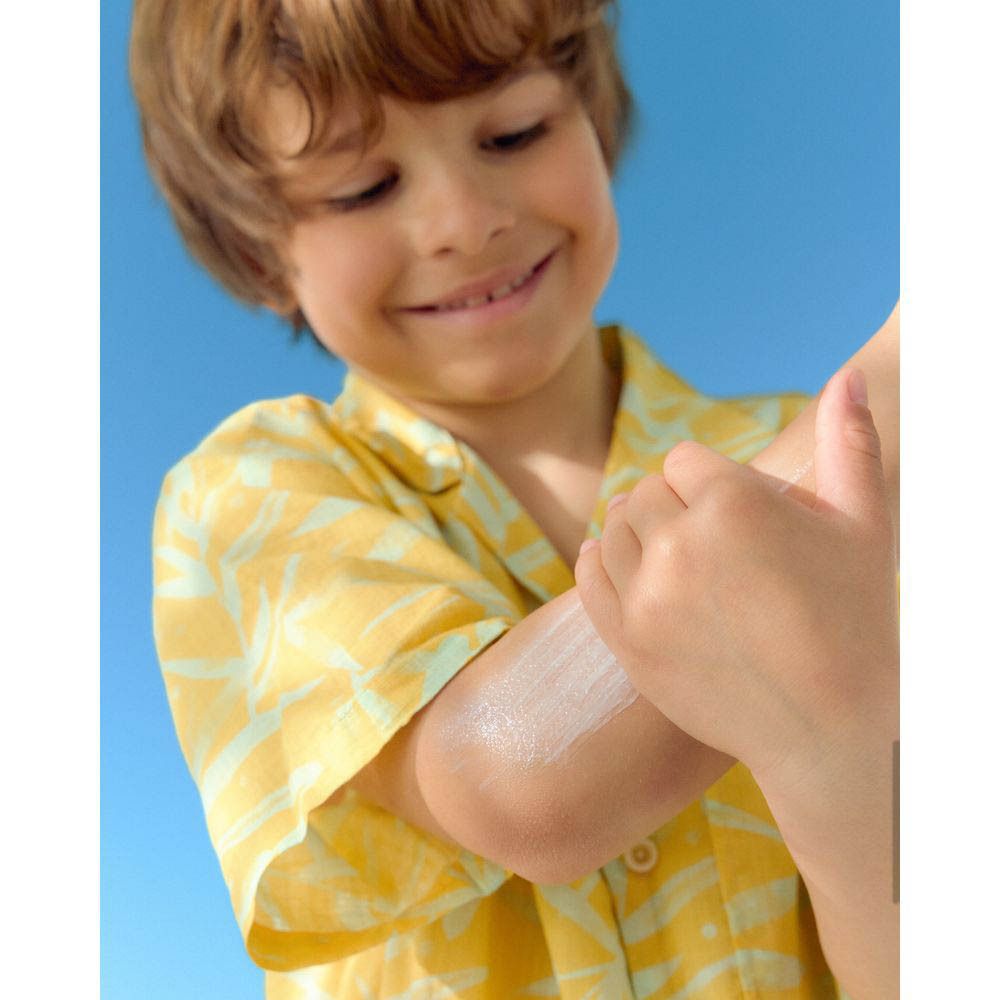 Enfant, bras frotté avec de la crème solaire. Chemise jaune.