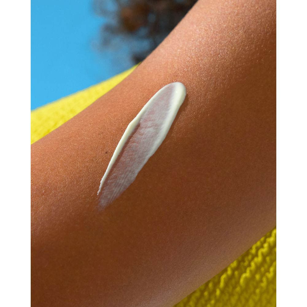 Crème After Sun appliquée sur le bras. Fond jaune.