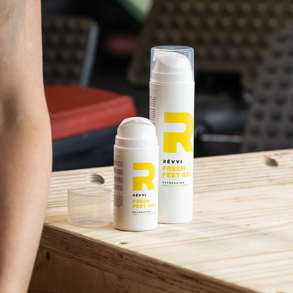 Deux flacons et un couvercle sur bois. Grand et petit flacon. Texte : RÉVVI FRESH FEET GEL. "R" jaune.