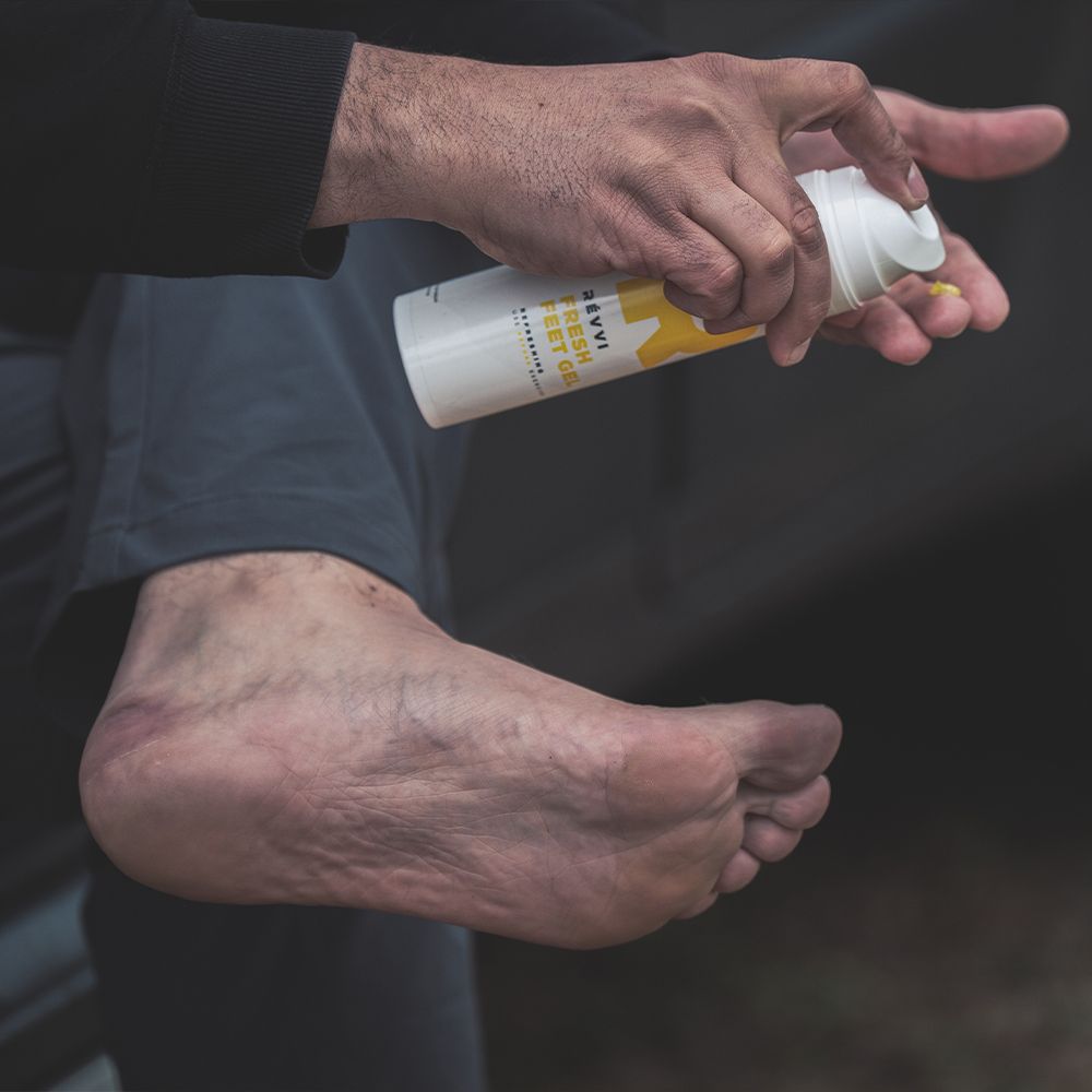 Personne tenant un flacon et appliquant du gel sur le pied. Flacon blanc avec "R" jaune. Texte : RÉVVI FRESH FEET GEL.