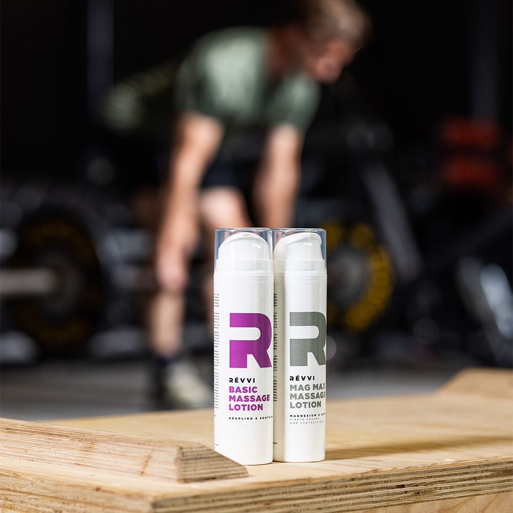 Deux flacons blancs avec logo rose et texte: RÉVVI Basic Massage Lotion. Sur surface en bois.