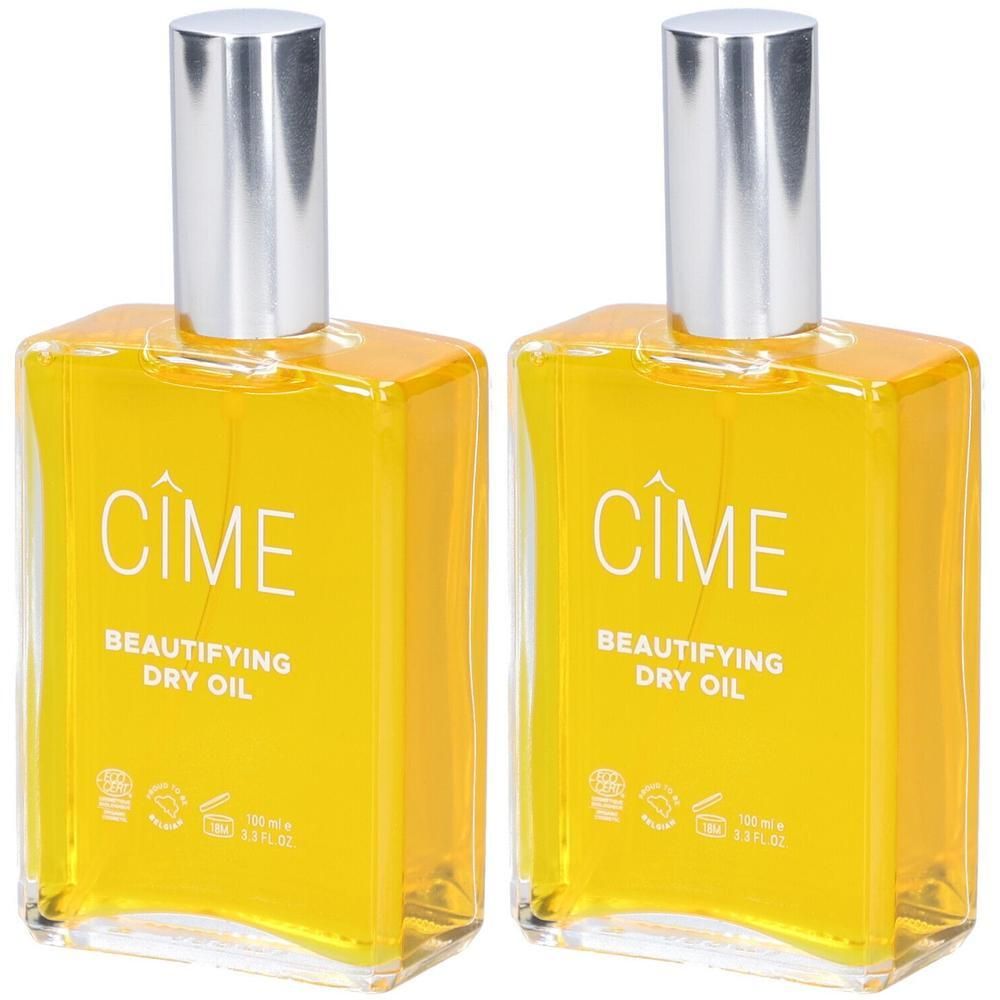 Deux flacons avec bouchons argentés. Inscription: Cîme, Beautifying Dry Oil. Liquide jaune dans des flacons carrés en verre.