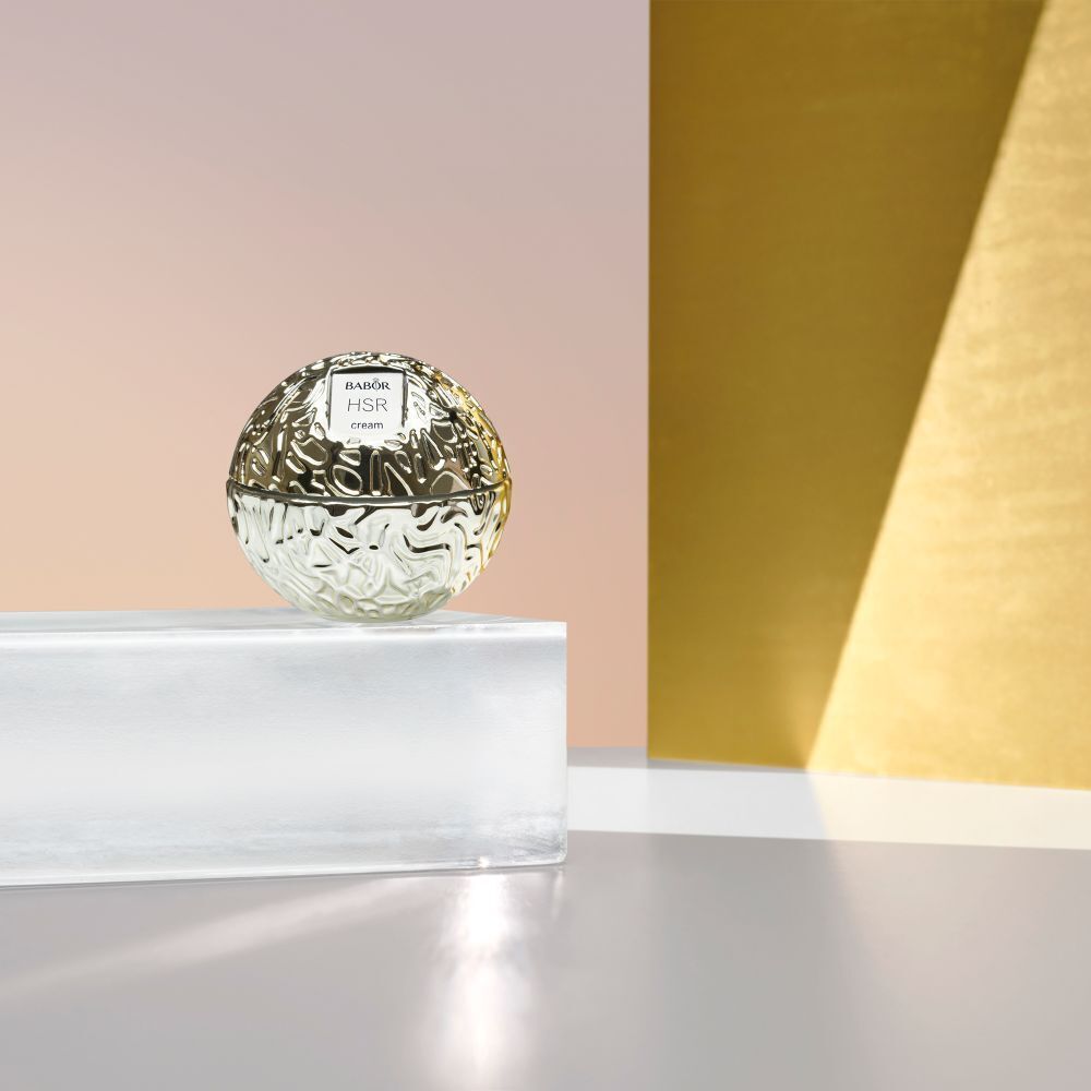 Pot Babor HSR Lifting Cream avec un échantillon de crème à côté sur une surface dorée.