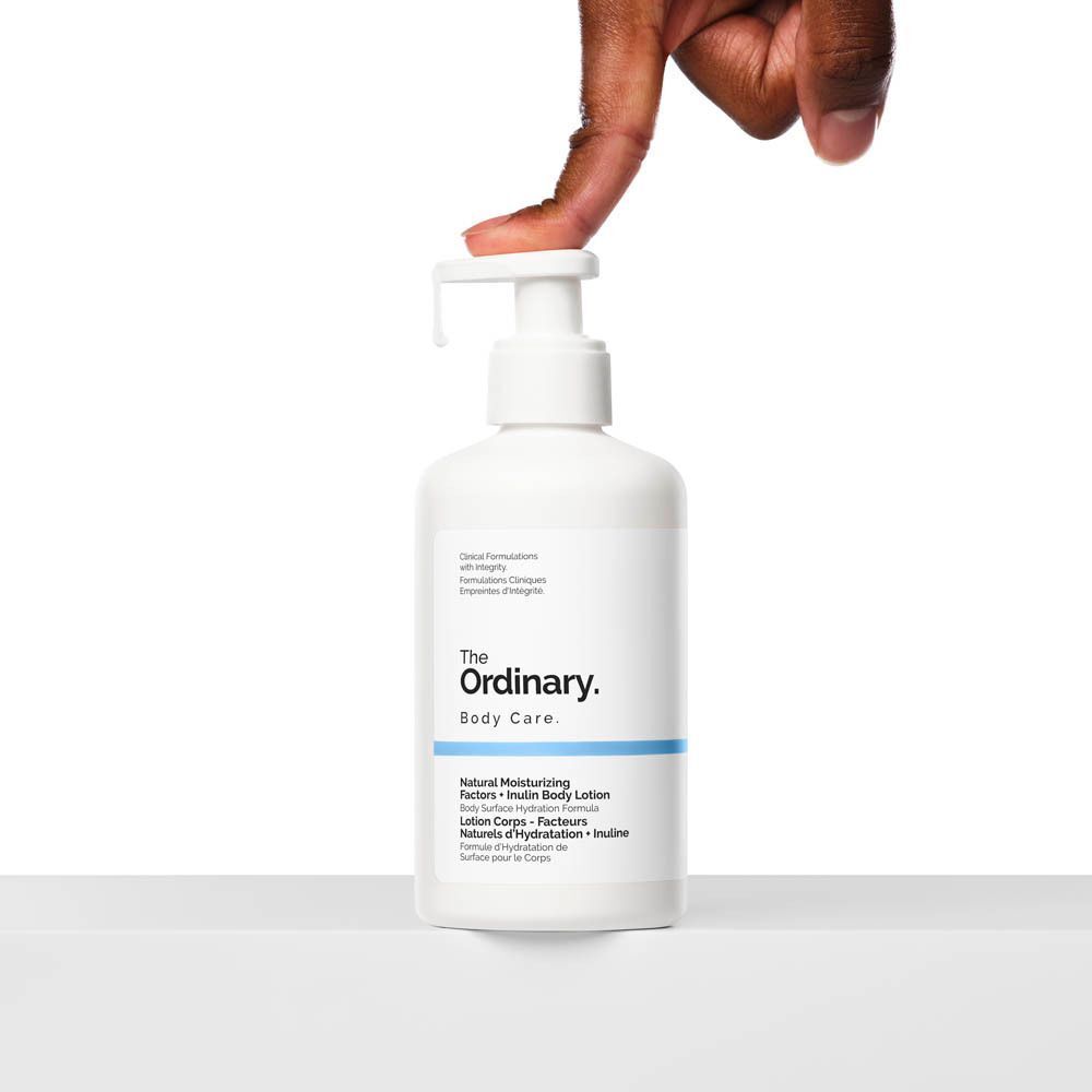 Flacon blanc avec pompe. Inscription : The Ordinary, Body Care, Natural Moisturizing Factors + Inulin Body Lotion. Main appuyant sur la pompe.