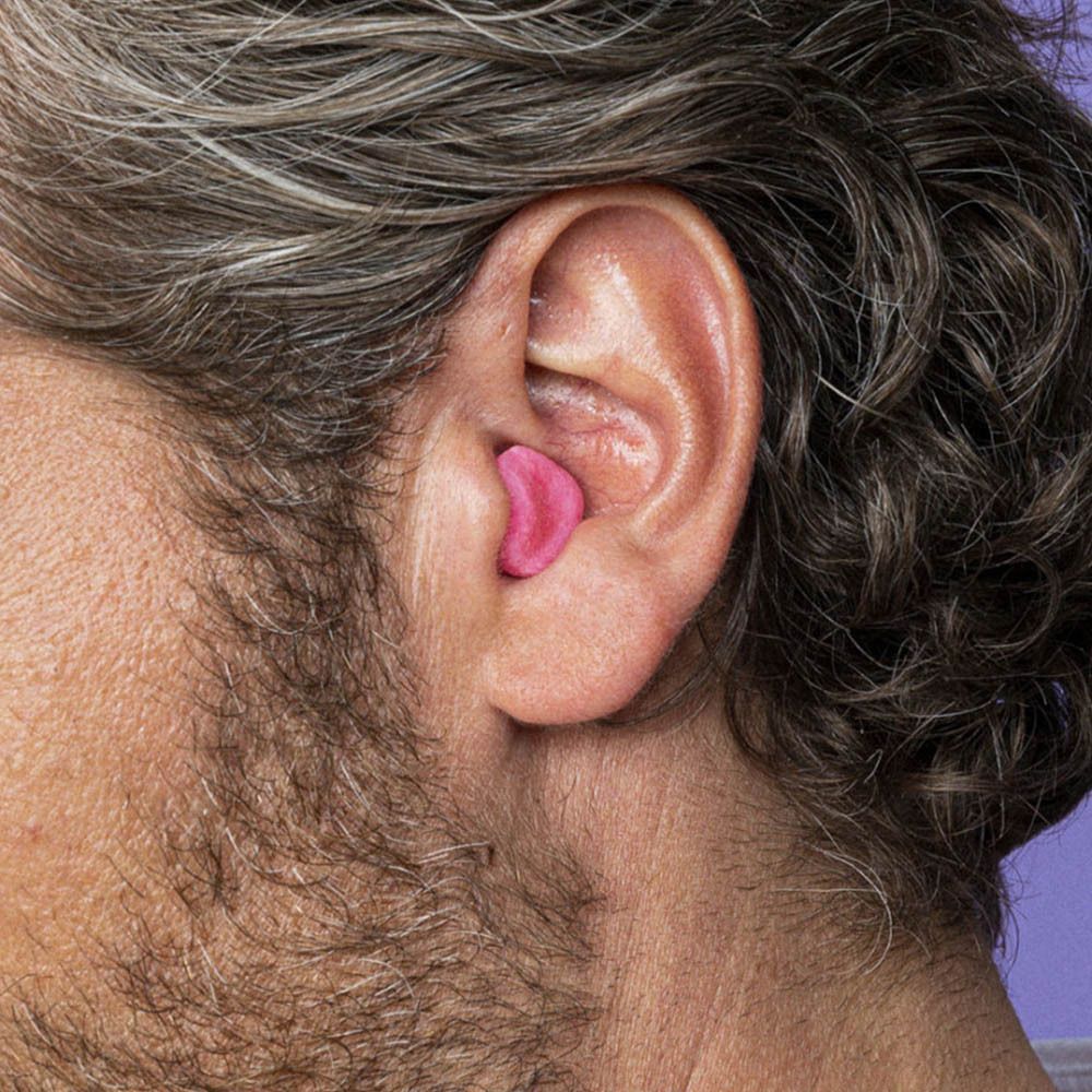 Un bouchon d'oreille en cire naturelle rose, taille medium, inséré dans une oreille humaine.